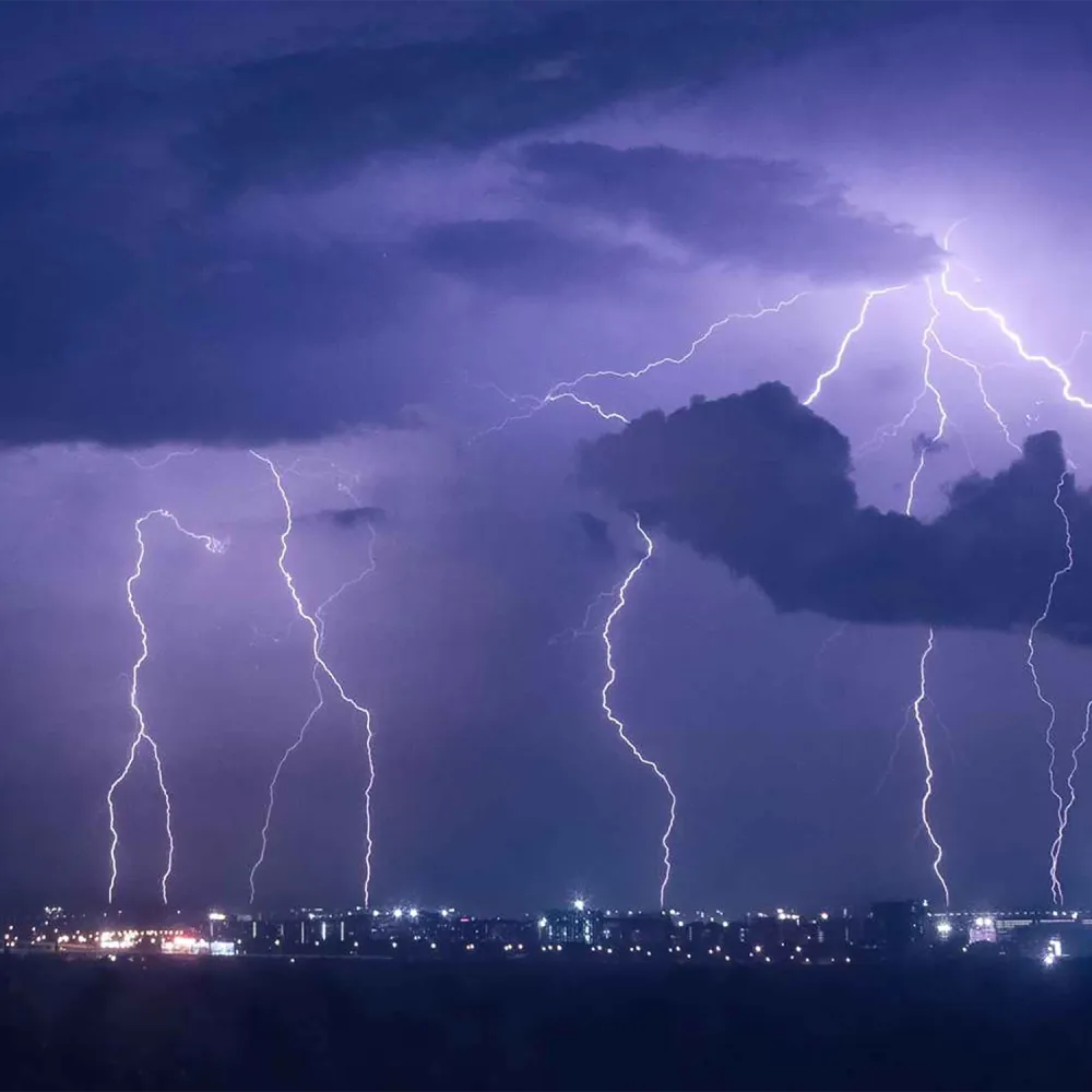 Multiple lightning bolts striking near a city skyline at night, with dark storm clouds illuminated by flashes of light.