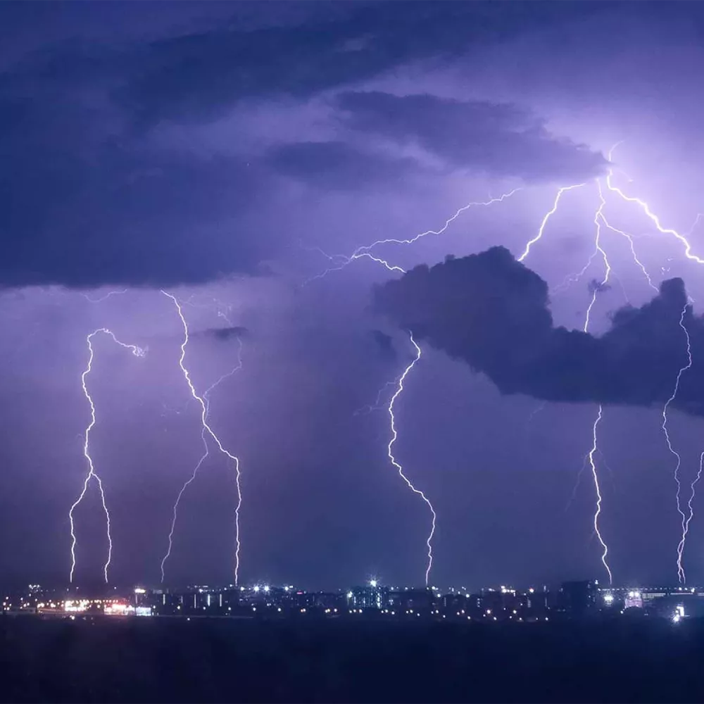 Multiple lightning bolts striking near a city skyline at night, with dark storm clouds illuminated by flashes of light.