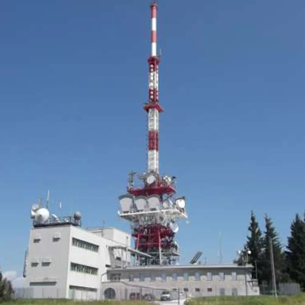 Tall red-and-white transmission tower with multiple antenna dishes beside a building, set against a clear blue sky.