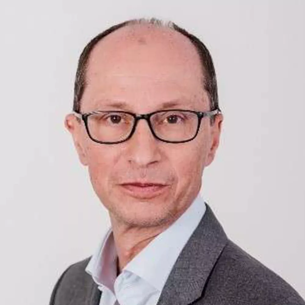 Portrait of a man wearing glasses, a gray jacket, and a light shirt against a white background.