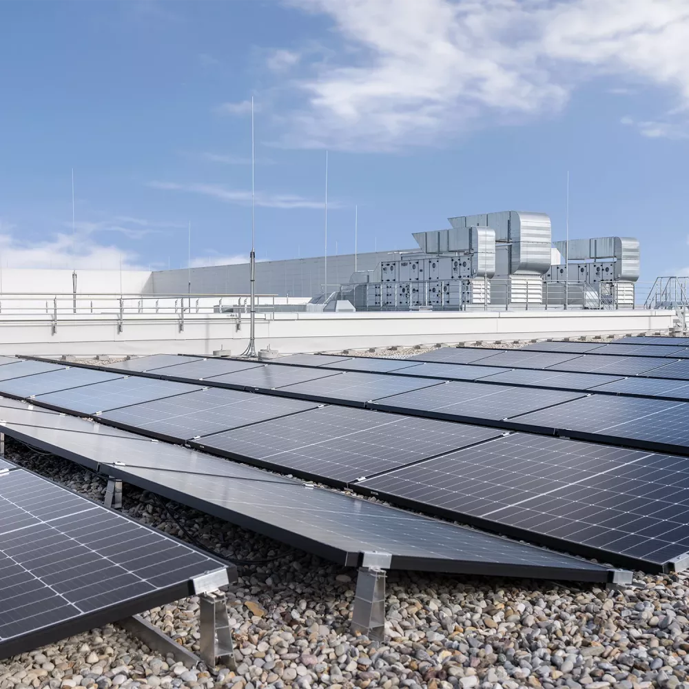 Industrial flat roof with photovoltaic panels, rooftop HVAC units, and lightning protection under a clear blue sky.