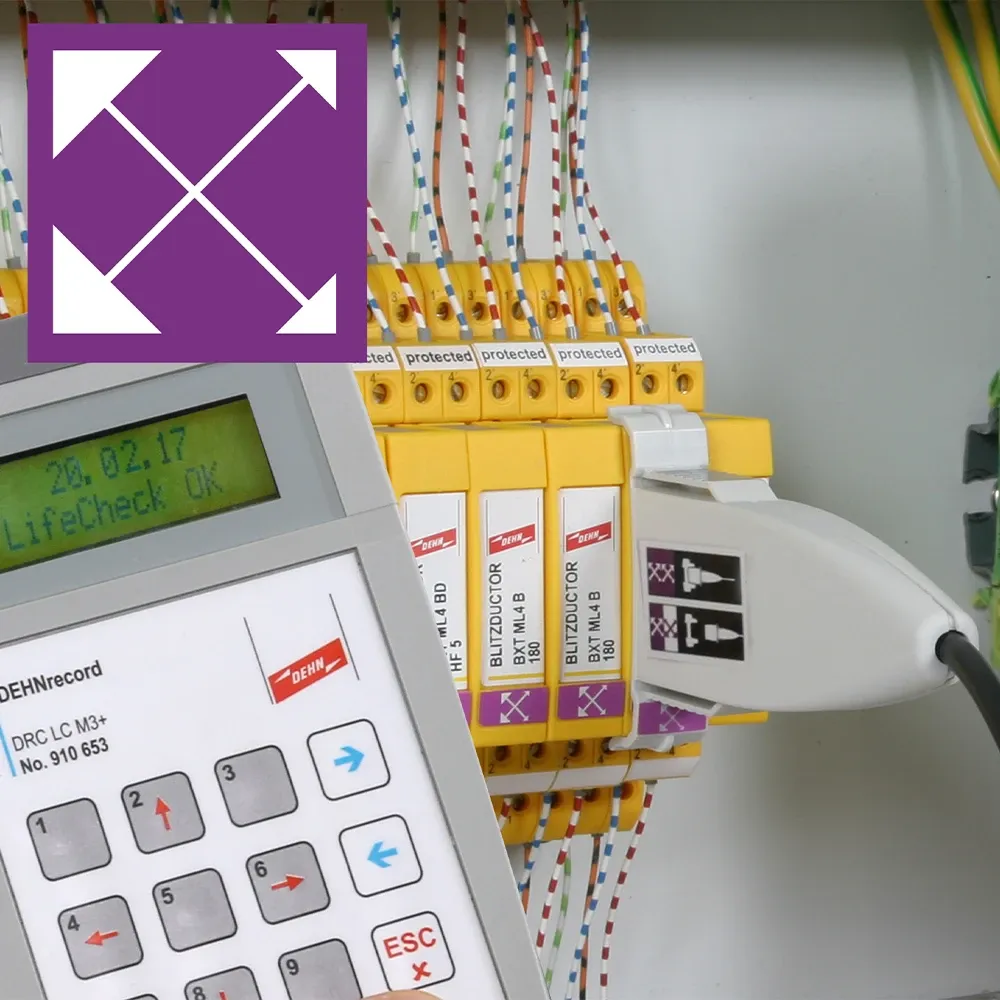 Electrical panel with yellow surge protection modules labeled “protected,” a handheld test device display, and a purple four-arrow symbol.