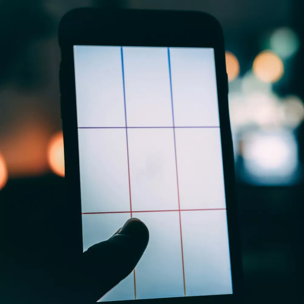 Finger touching a smartphone screen displaying a grid of colored lines, with blurred lights in the background.