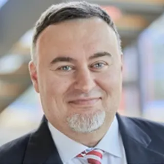 Portrait of a man with short dark hair and gray goatee, wearing a suit and red striped tie, smiling at the camera