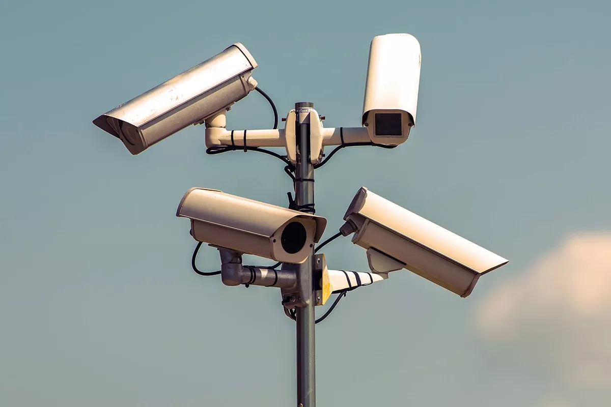 Outdoor surveillance pole with multiple security cameras mounted in different directions against a clear sky.