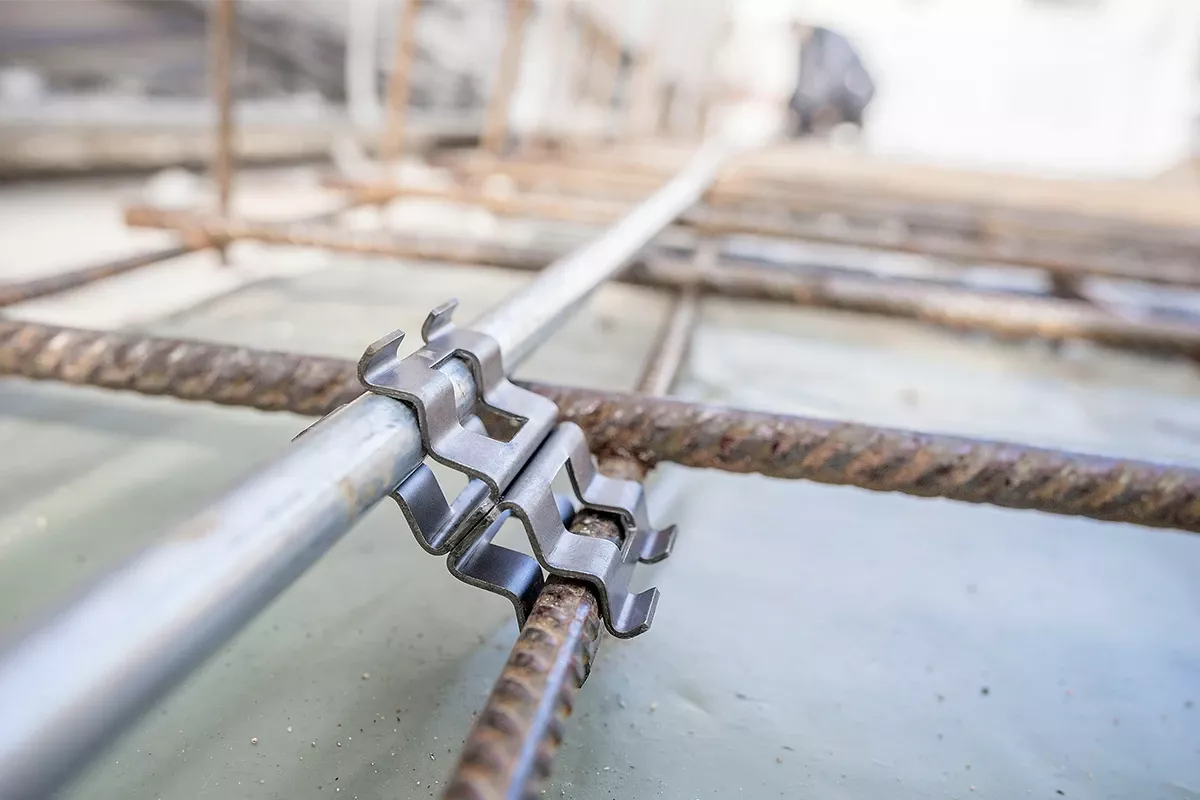Close-up of a metal grounding clamp connecting a steel conductor to reinforcing rebar embedded in a concrete foundation slab.